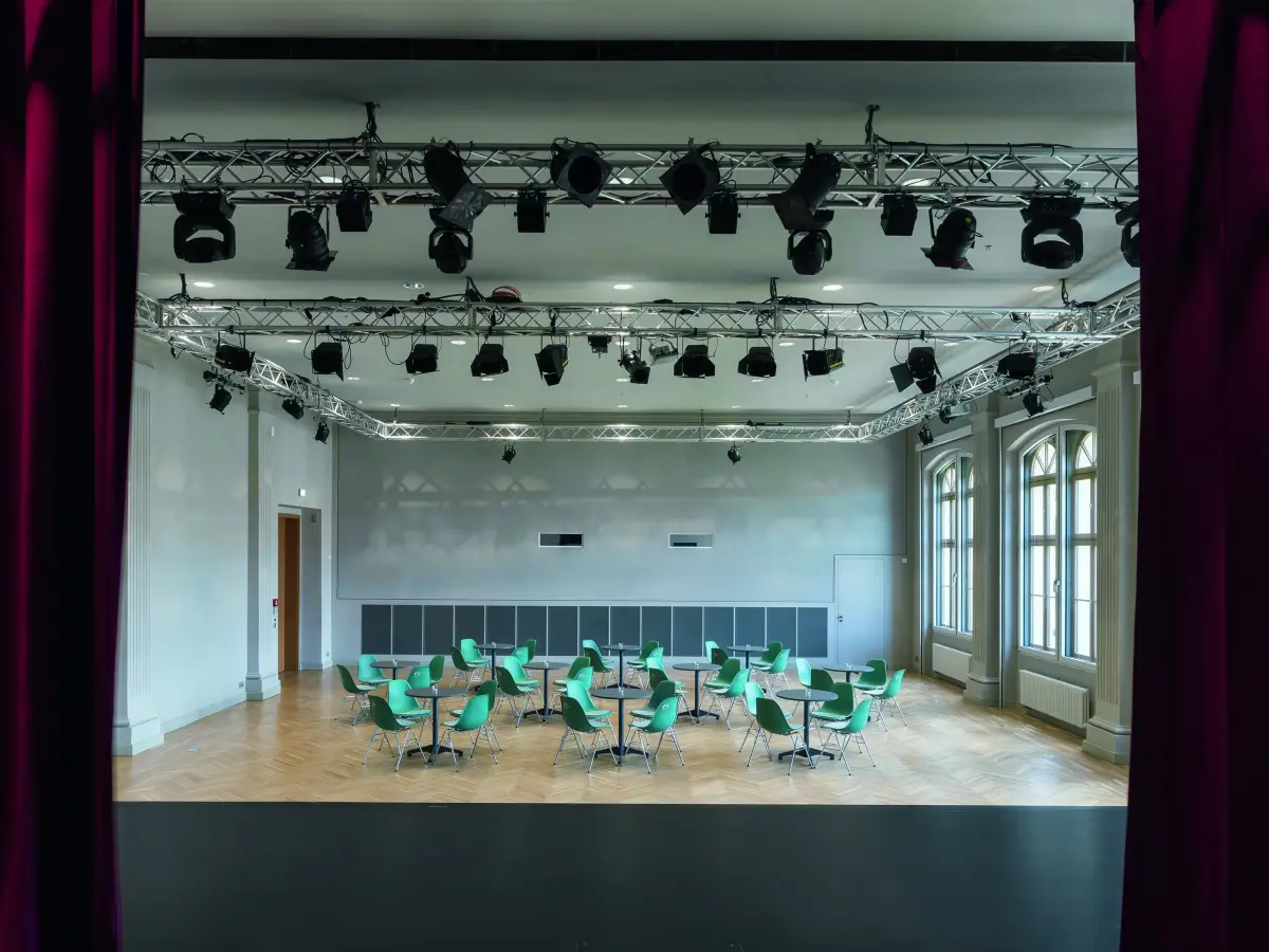 Blick durch die Samtvorhänge auf der Bühne in den Ballsaal mit Tischen und Stühlen