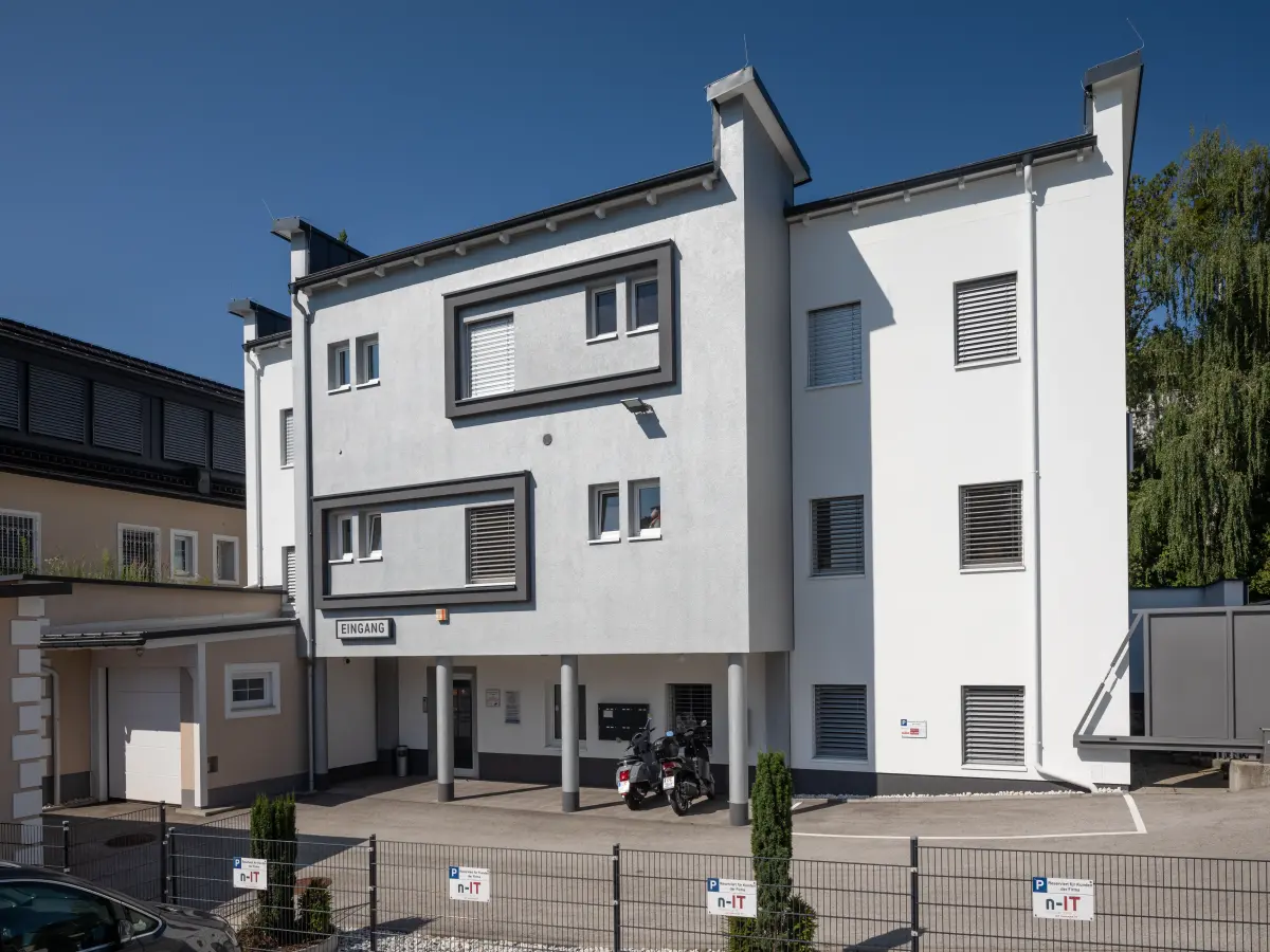Moderne weiße Fassade mit grauen Akzenten, rechteckigen Fenstern, Rollläden und gekennzeichnetem Eingang.