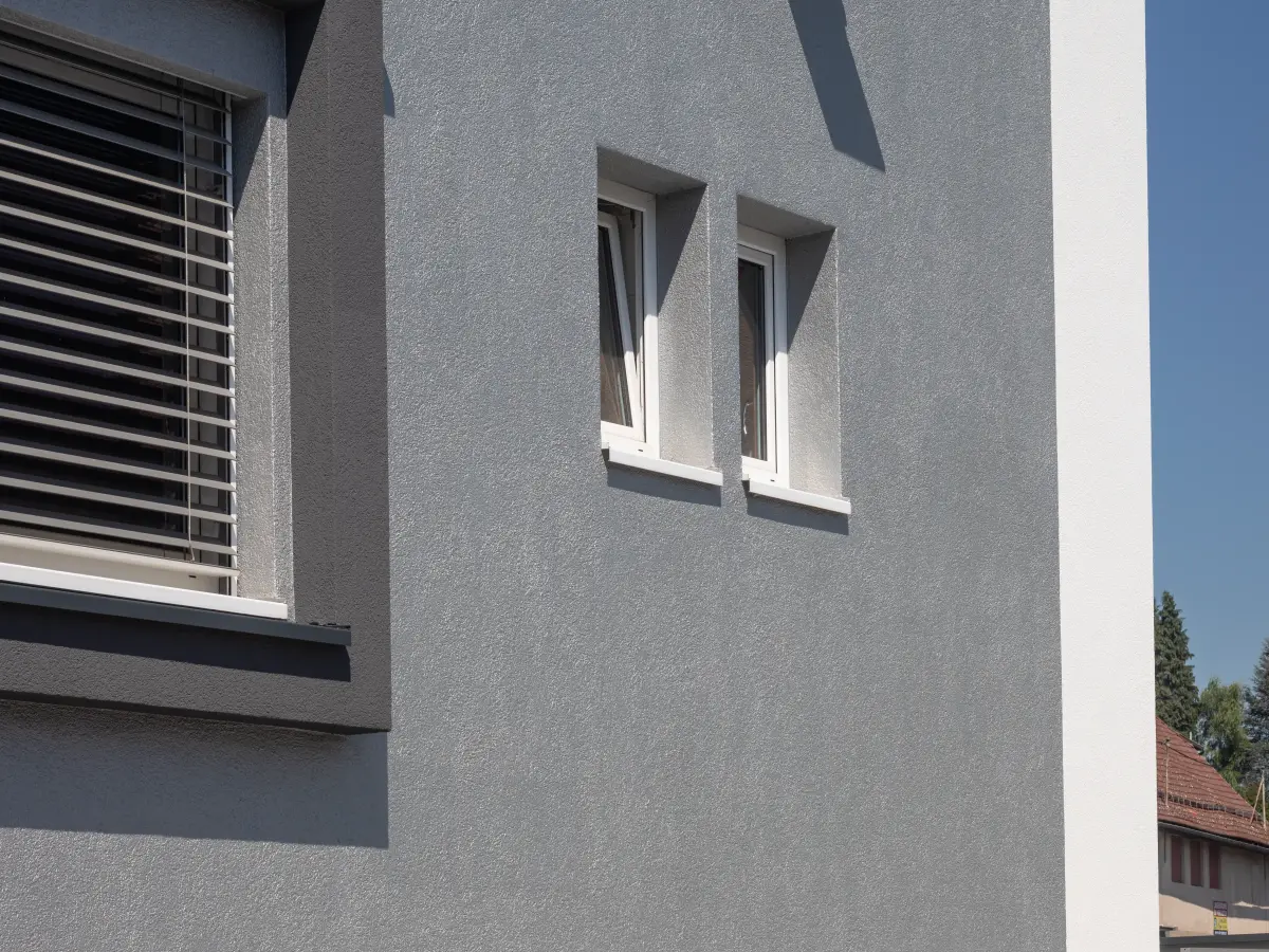 Fassadendetail mit grauer Oberfläche, modernen Fenstern und integriertem Sonnenschutz.