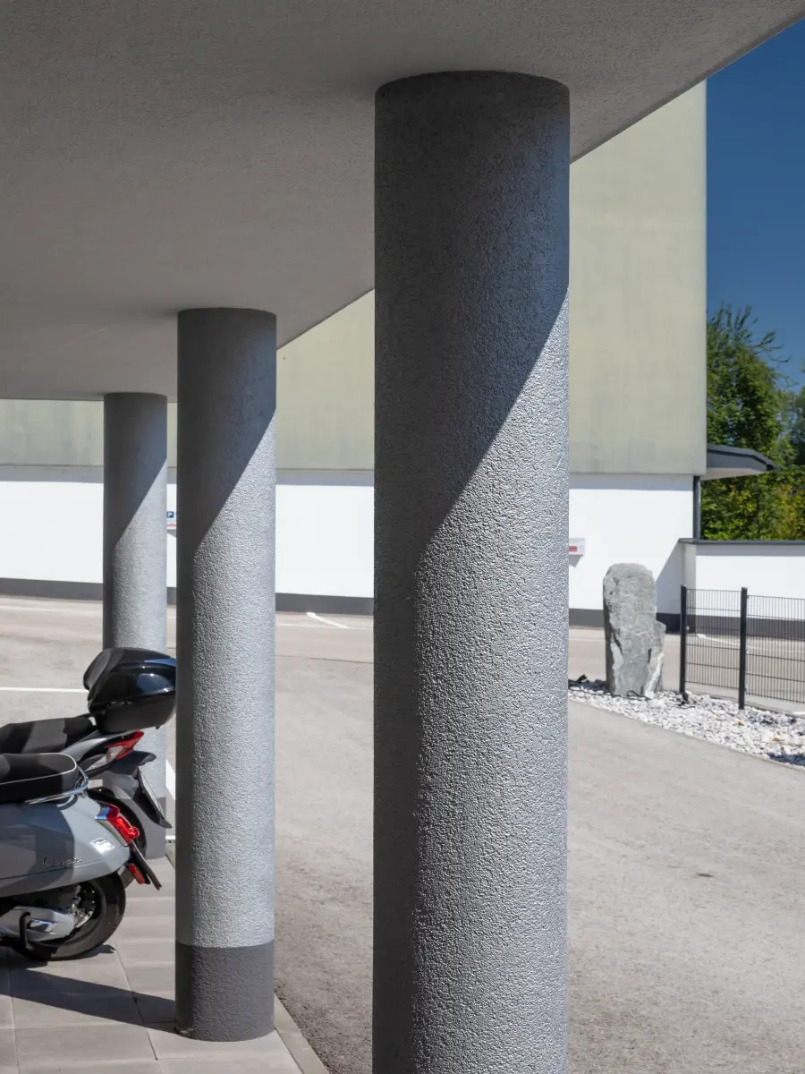 Detailansicht grauer Säulen eines überdachten Eingangsbereichs mit geparktem Roller.