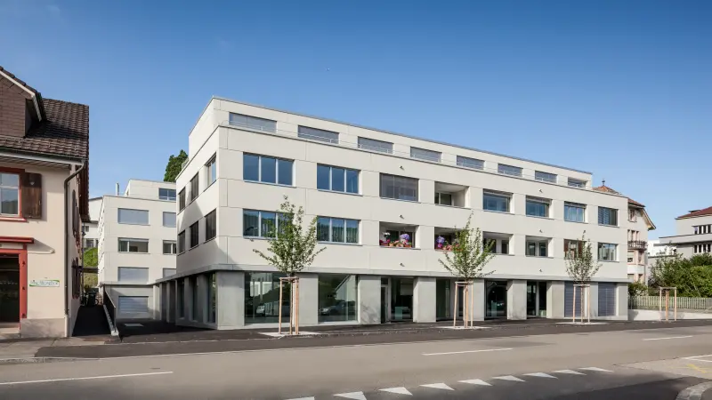 Modernes Wohngebäude mit großen Fenstern und Balkonen an einer Straße bei klarem Himmel.