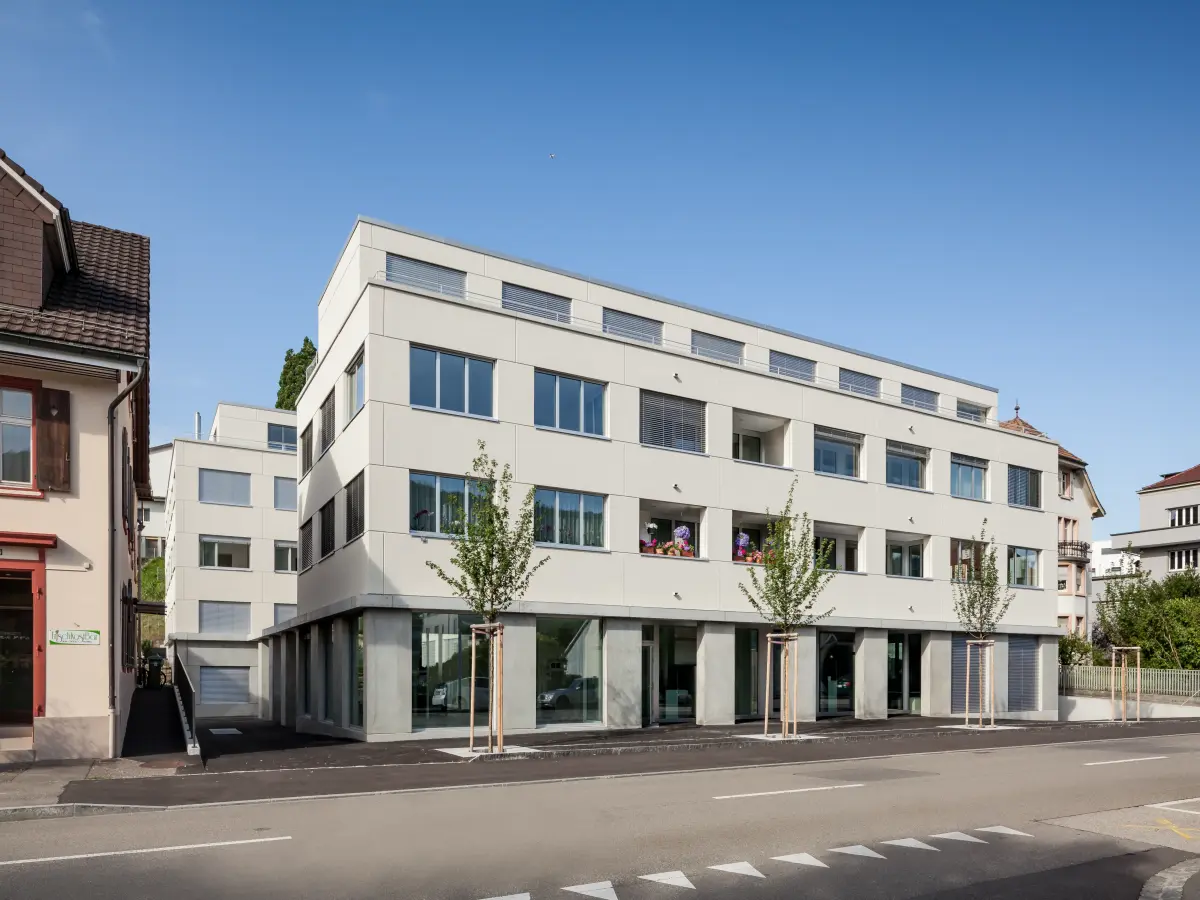 Modernes Wohngebäude mit großen Fenstern und Balkonen an einer Straße bei klarem Himmel.