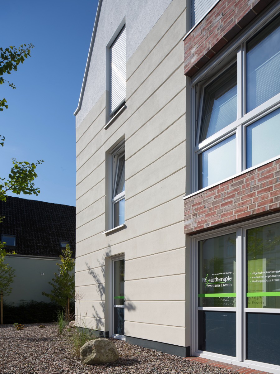 Hochaufragende, schlichte Gebäudefassade in Beige mit großflächigen Fenstern und einem Sockel aus Ziegeln.
