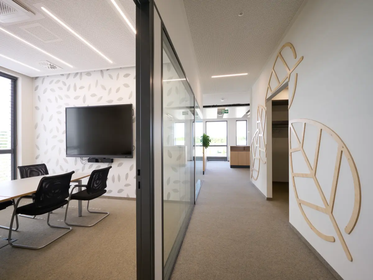 Interno moderno di uffici con sala riunioni vetrata, decorazioni a foglia sulle pareti e luce naturale.