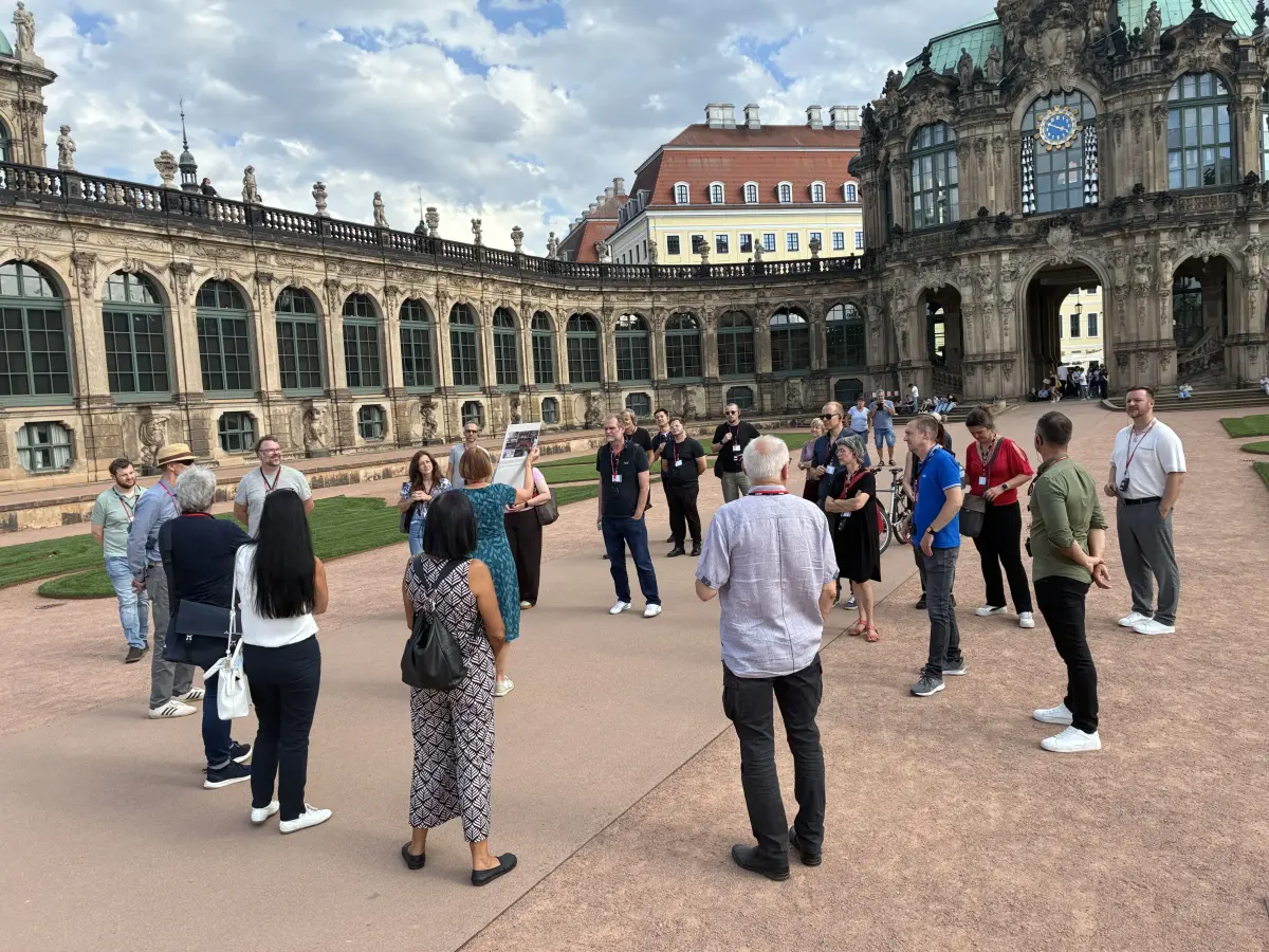 Eine Gruppe von Menschen steht bei einer Führung im Dresdner Zwingerhof vor der barocken Bogengalerie und dem Kronentor.