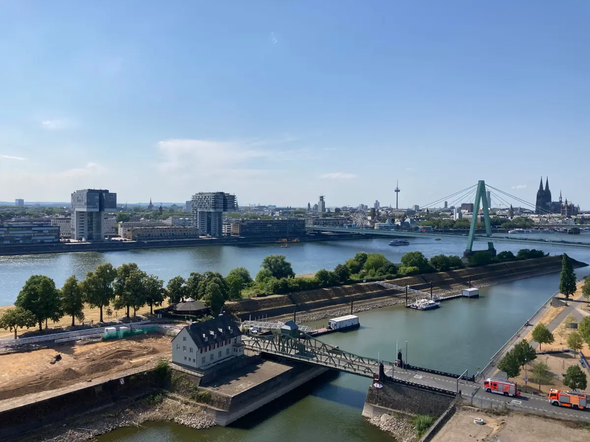 Blick über den Rhein in Köln mit Dom und Fernmeldeturm am Horizont.