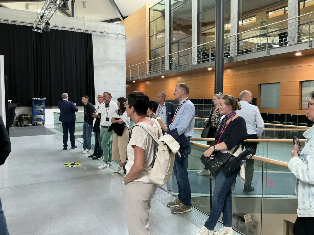 Gruppe im großen Foyer mit Holzverkleidung, Glasbrüstung und Sichtbetonwand.