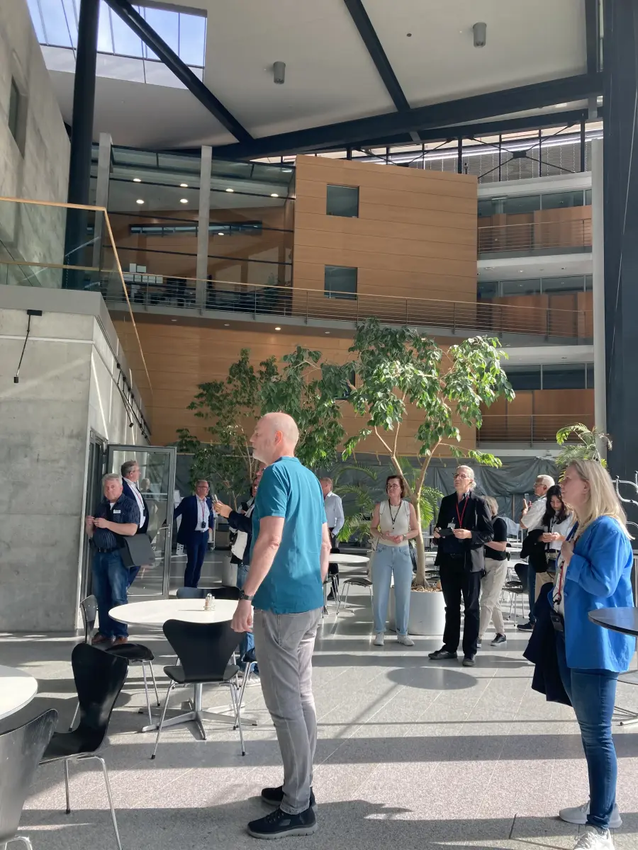 Helles Atrium mit sichtbaren Stahlträgern, Sichtbeton, holzverkleideten Galerien und Personen.