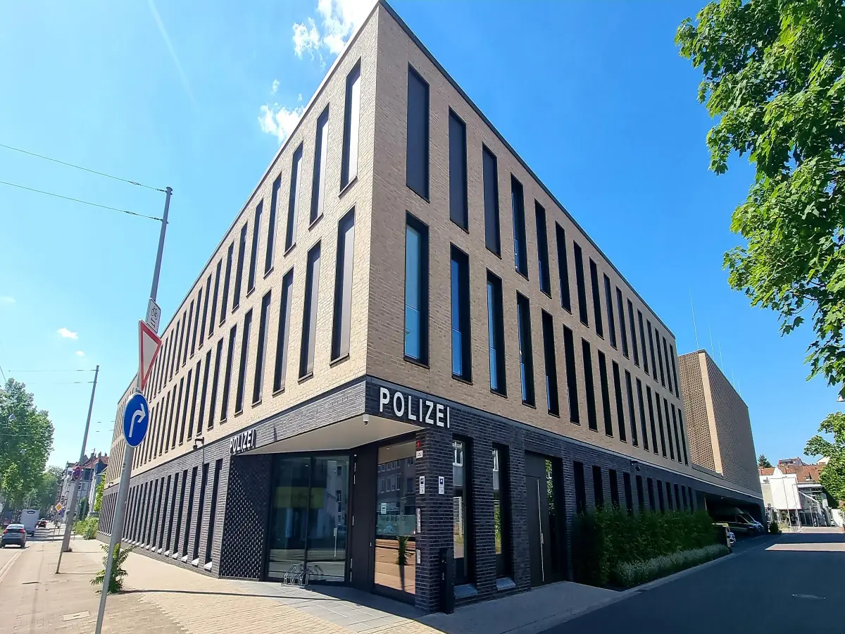Moderne Polizeiwache mit großem "POLIZEI"-Schriftzug, schmalen Fenstern und blauem Himmel.