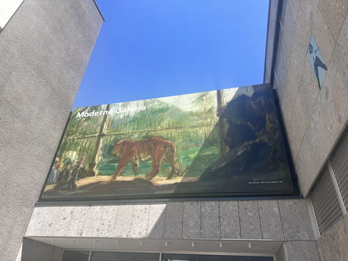 Banner mit der Aufschrift „Moderne Galerie“ über dem Eingang, zeigt eine expressionistische Darstellung eines großen braunen Tieres vor grüner Landschaft und blauem Himmel.