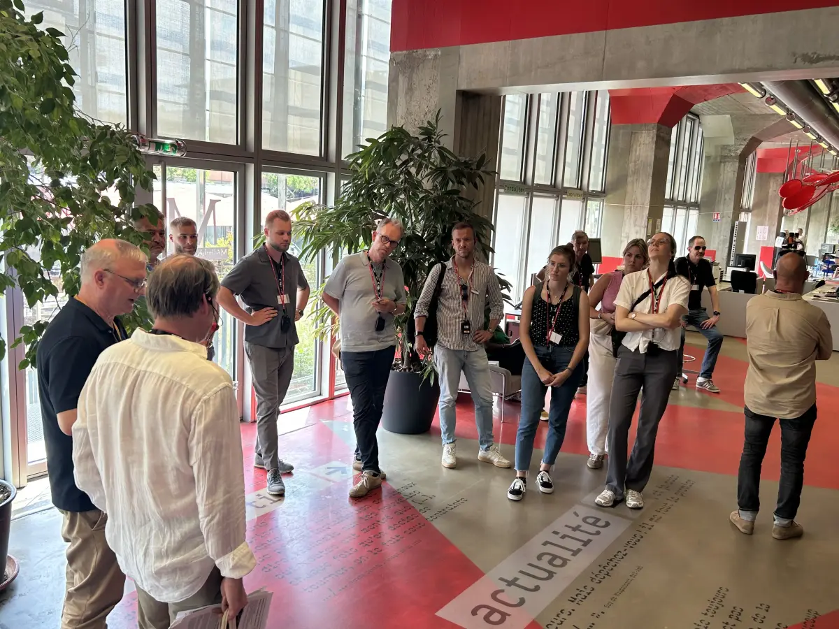 Helles, industriell-modernes Foyer mit großen Fenstern, Sichtbeton, roten Akzenten und einer stehenden Besuchergruppe.