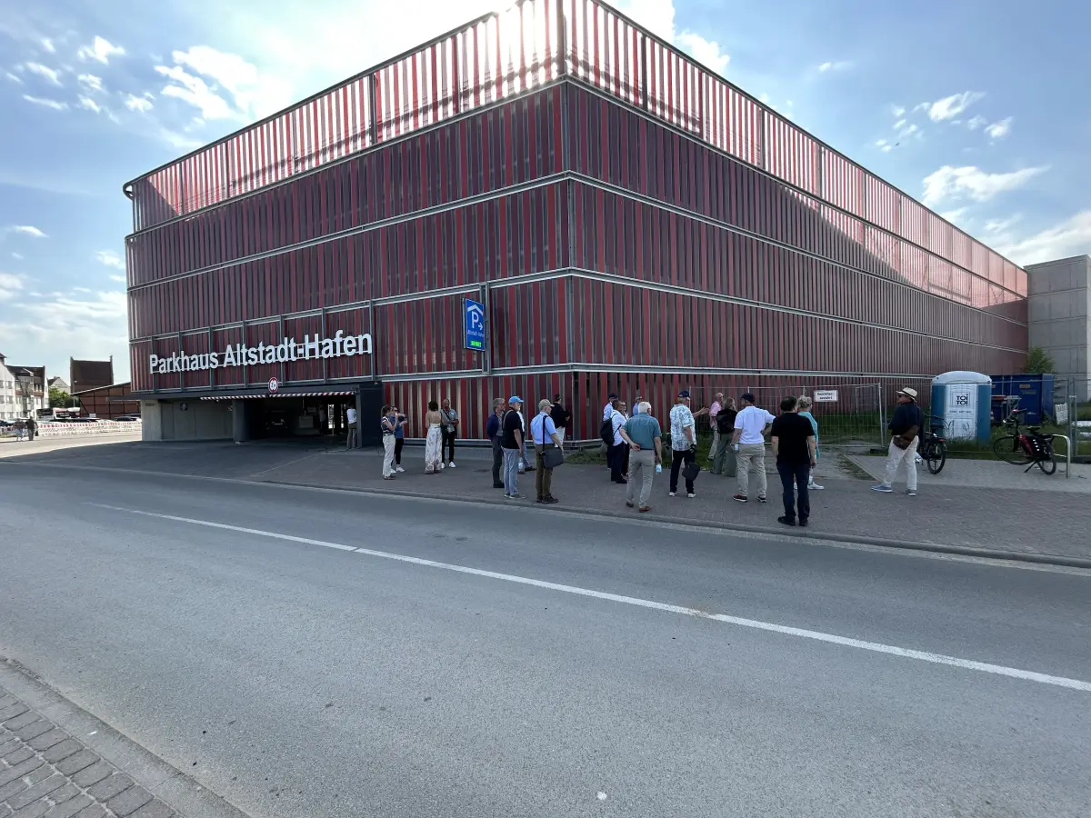 Großes Parkhaus „Altstadt-Hafen“ aus roten Lamellen, davor steht eine Gruppe von Menschen am Straßenrand.