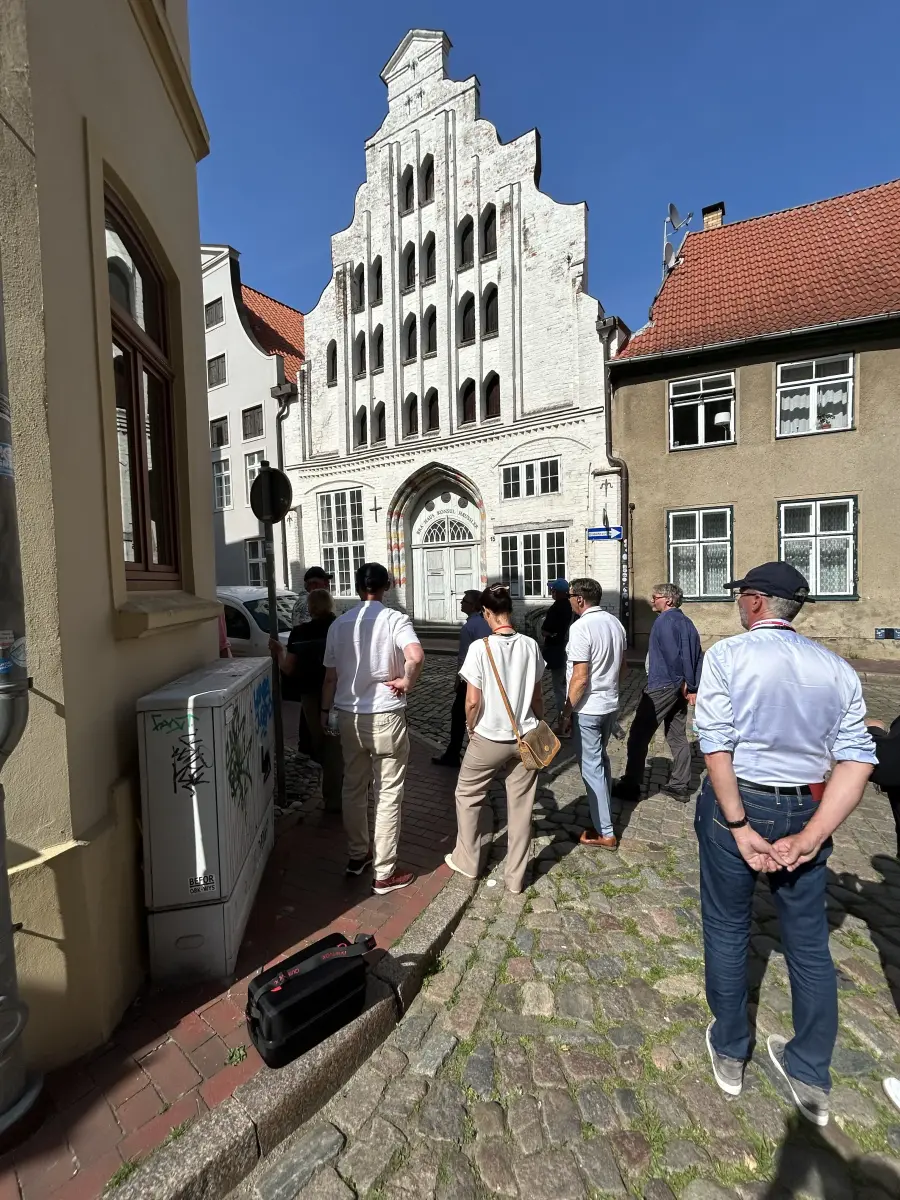 Gruppe von Personen bei einer Führung in einer schmalen Altstadtgasse vor einem historischen weißen Giebelhaus.