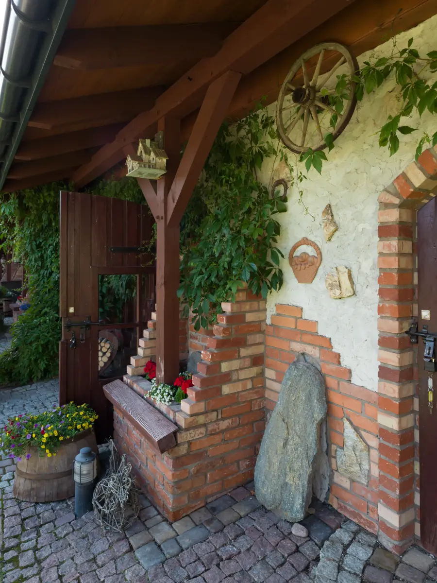 Rustikale Hausecke mit Pflanzen, Backsteinmauer und dekorativen Elementen.