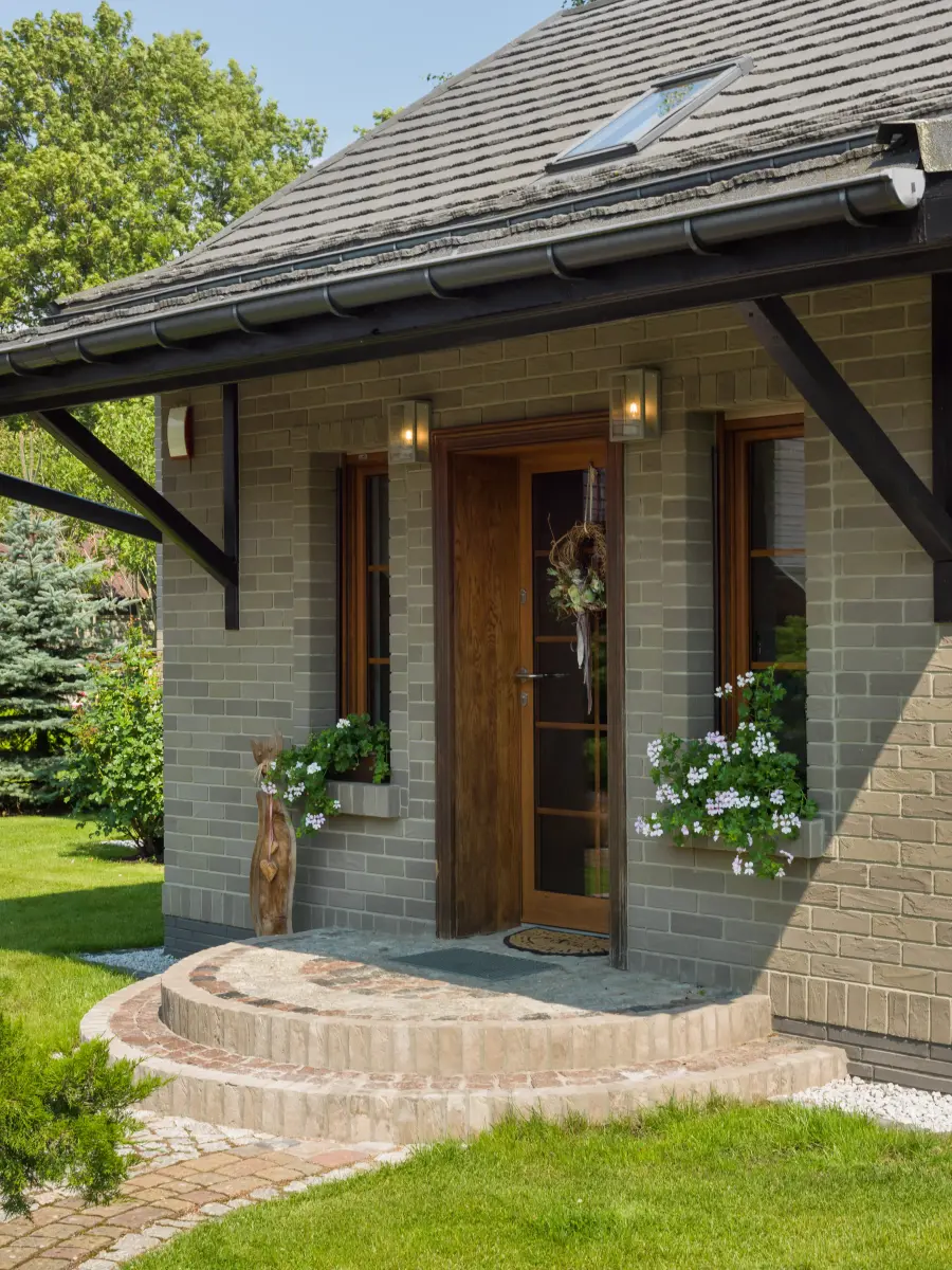 Eingangstür eines Hauses mit Blumen in Blumenkästen und rundem Stufenpodest.