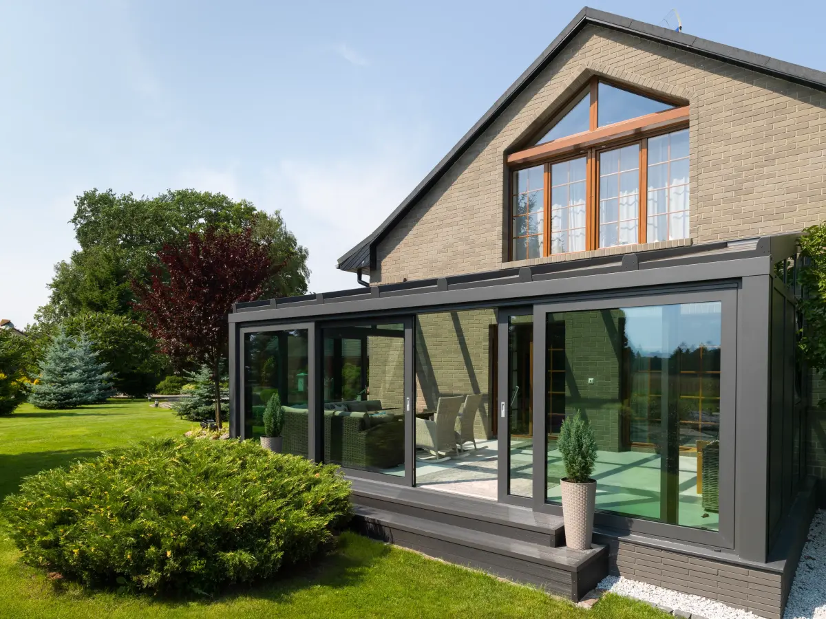 Haus mit moderner Glasveranda und Garten bei Sonnenschein.