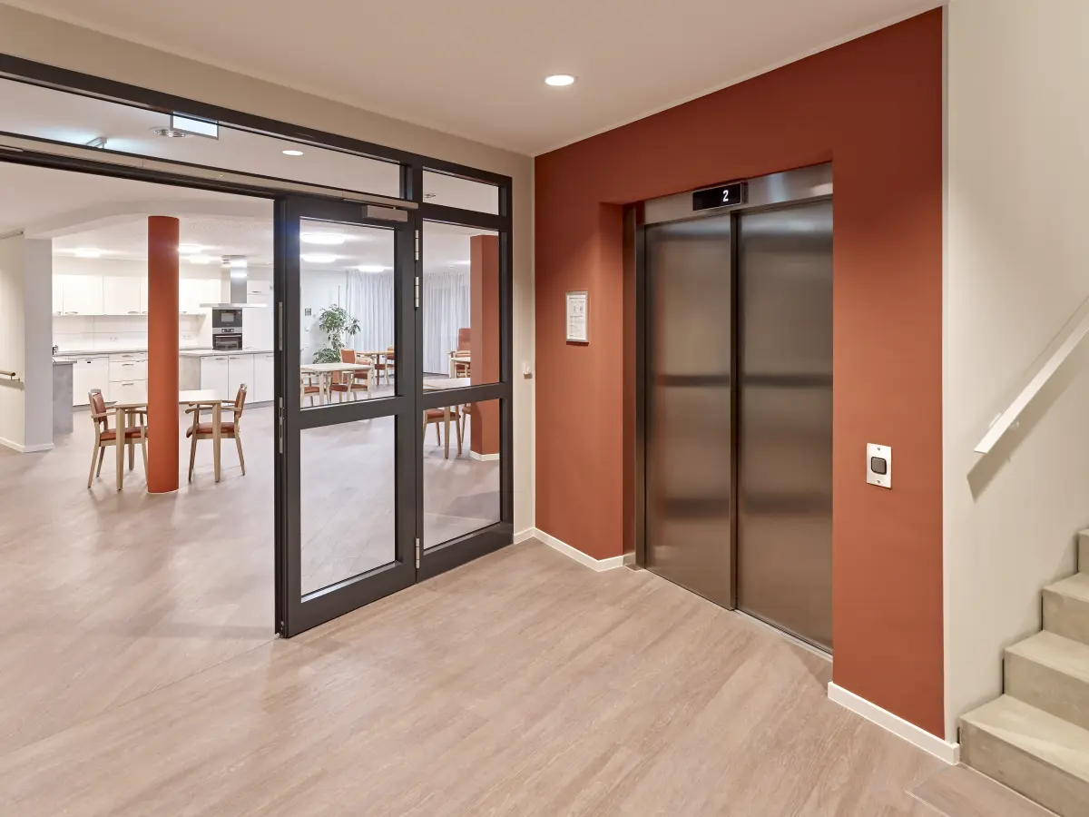 Interieur eines Seniorenheims mit orangefarbenen und weißen Wänden und einem Aufzug