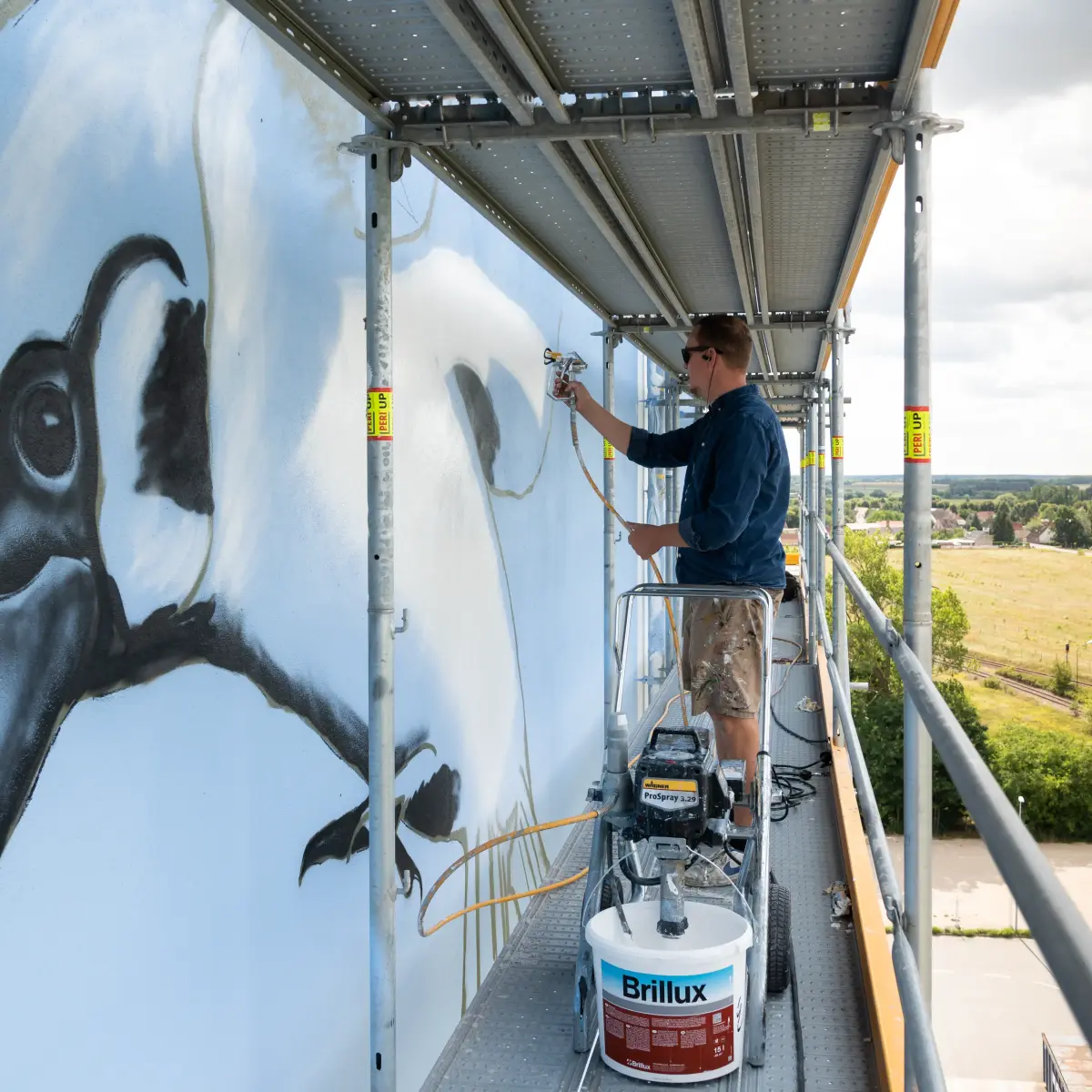 Seitenansicht Künstler auf Gerüst mit Brillux Farben