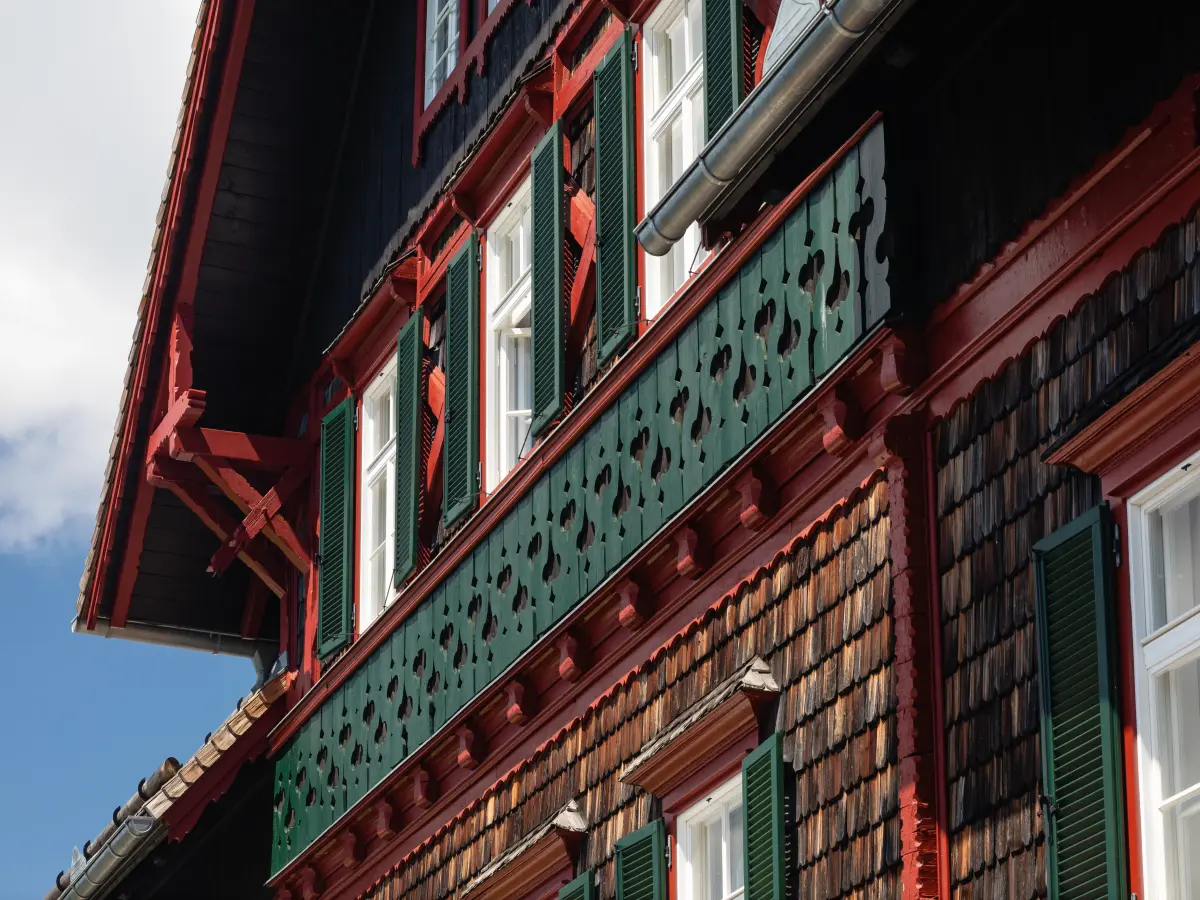 Detailansicht der aufwendig gestalteten Holzfassade des Stubenberghauses mit grünen Fensterläden, roten Holzakzenten und einem kunstvoll verzierten Holzbalkon.