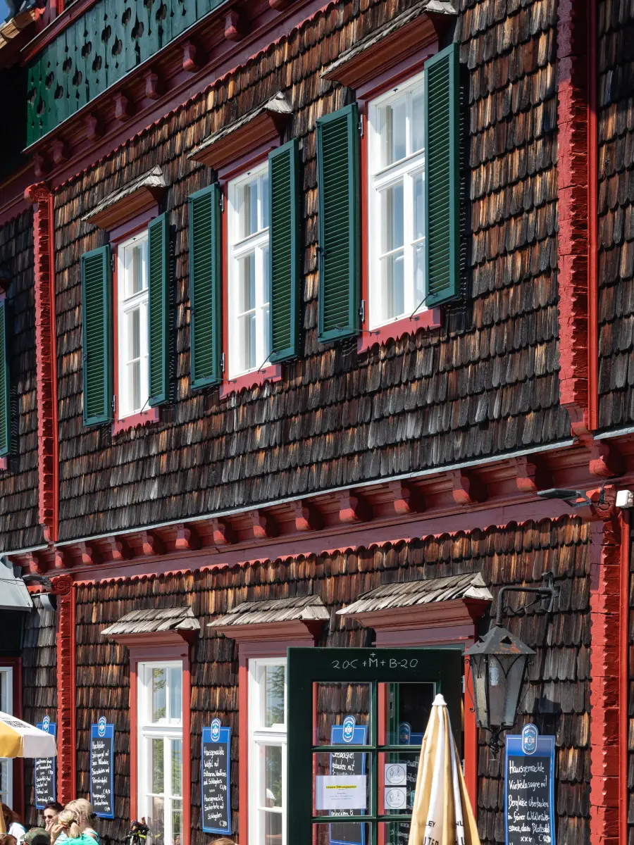 Detailansicht der Holzfassade des Stubenberghauses mit grün gestrichenen Fensterläden, roten Zierleisten und Schindelverkleidung.