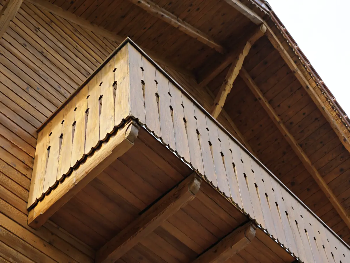 Detailansicht eines hölzernen Balkons mit dekorativen Elementen und sichtbarer Dachkonstruktion.