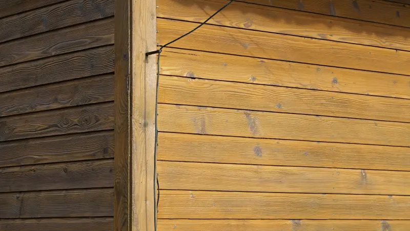 Holzwand mit hellen und dunklen Brettern, Kabel an der Ecke.