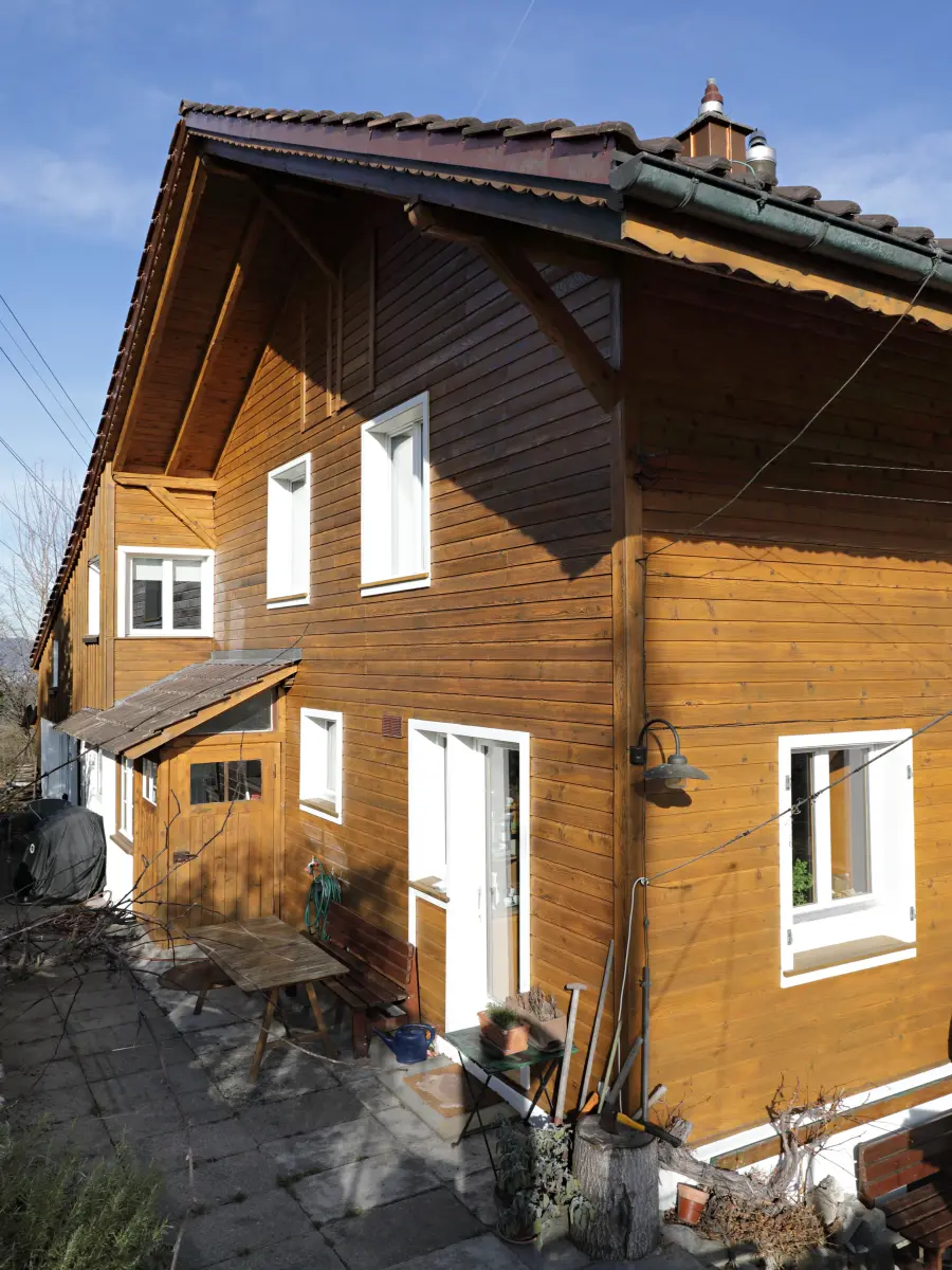 Seitenansicht eines Holzhauses mit Satteldach und weiß gerahmten Fenstern.