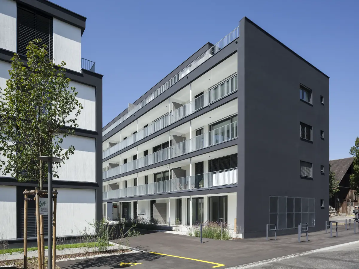 Moderne Wohnanlage mit dunklen und weißen Fassaden, großzügigen Balkonen und begrünten Außenbereichen, bei klarem Himmel.