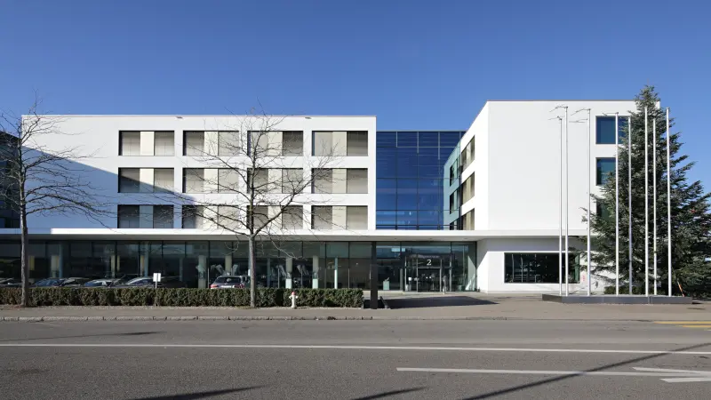 Modernes Gebäude mit weißer Fassade, großen Fenstern und Glaselementen, aufgenommen bei klarem Himmel.