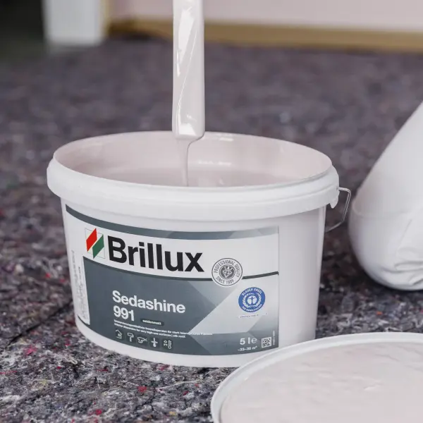 Pinsel mit weißer Farbe über einem Eimer Brillux Sedashine 991 auf einem Abdeckvlies.