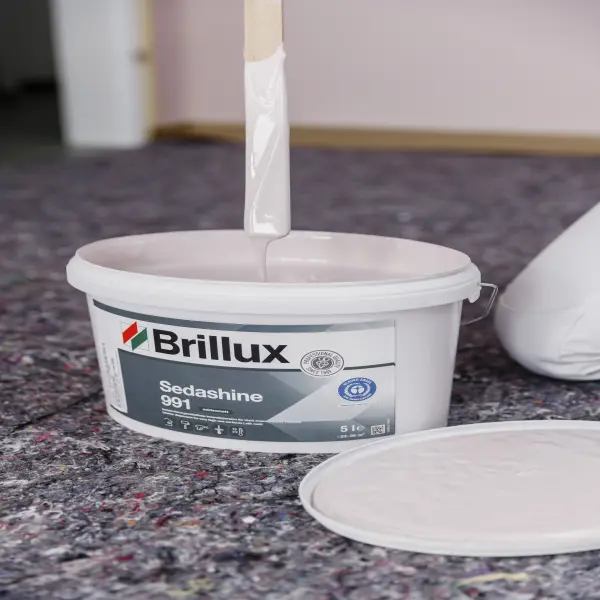 Pinsel mit weißer Farbe über einem Eimer Brillux Sedashine 991 auf einem Abdeckvlies.