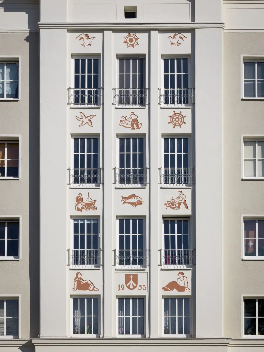 graue Fassade mit roten Illustartionen an der Wand zwischen den Fenstern