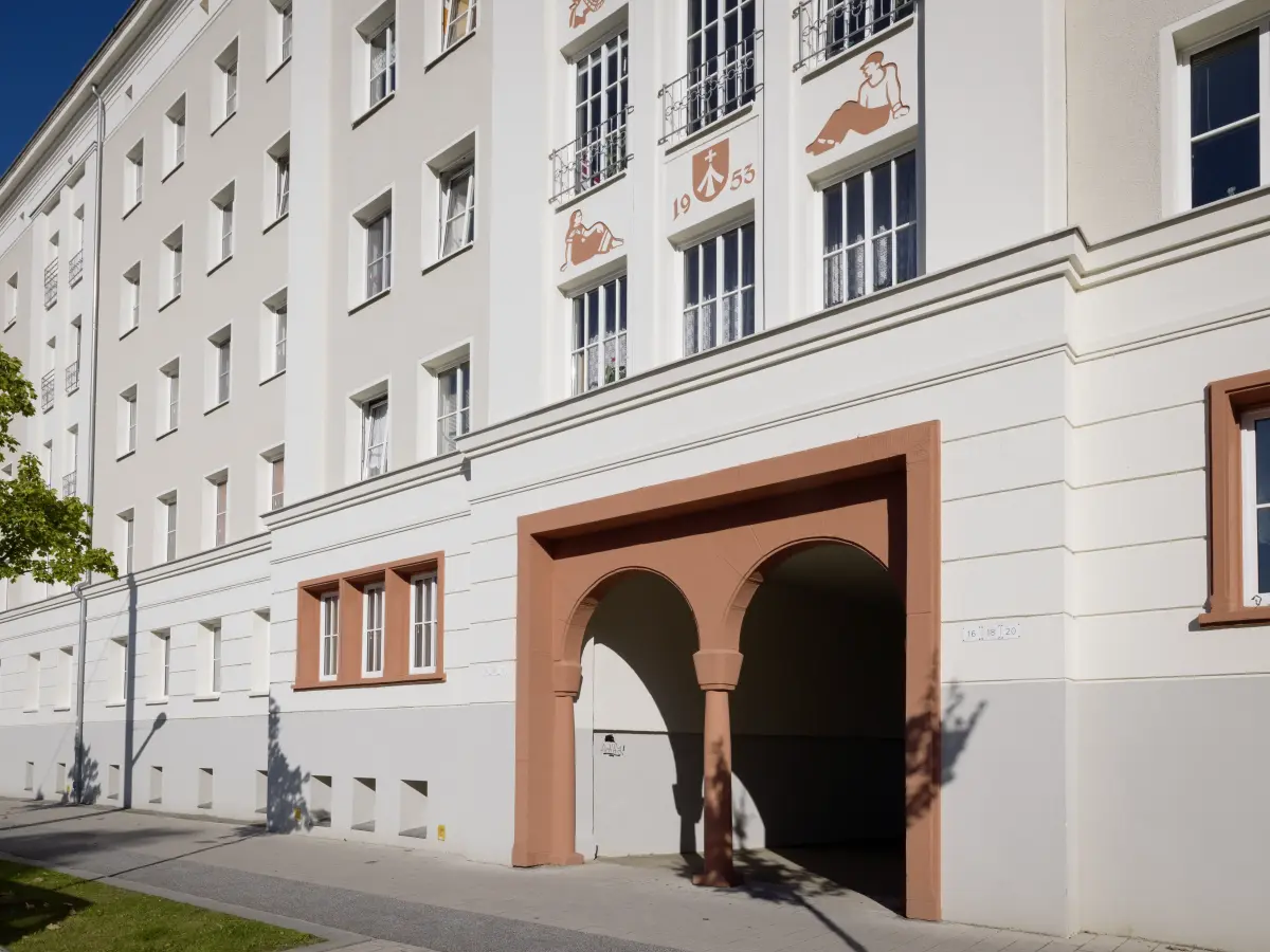 Akzente setzt ein erdiges Rot. Es hebt bauliche Details und prägnante Bildsymbole der Fassade hervor.