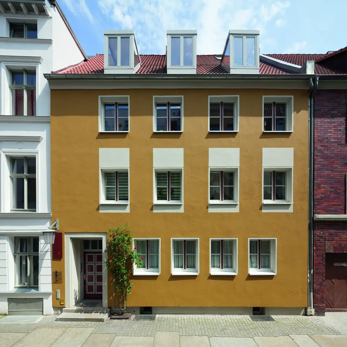 Goldockerfarbene Fassade mit weißen Fensterrahmen 