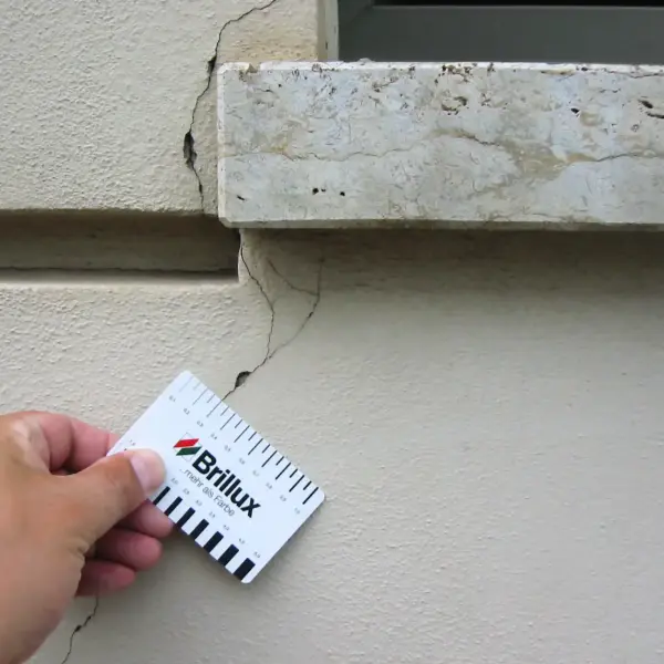 Hand hält eine Brillux Messkarte an ein Risskante einer Wandmauer
