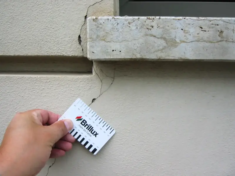 Hand hält eine Brillux Messkarte an ein Risskante einer Wandmauer