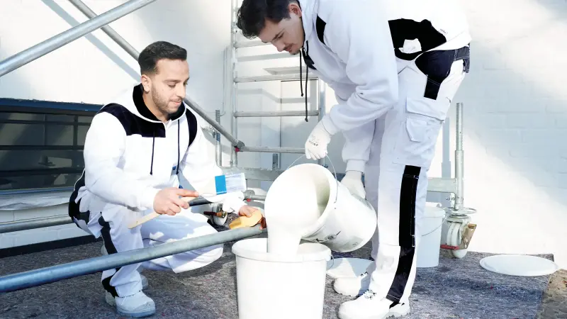 Zwei junge Maler stehen auf einer Baustelle und topfen Farbe um