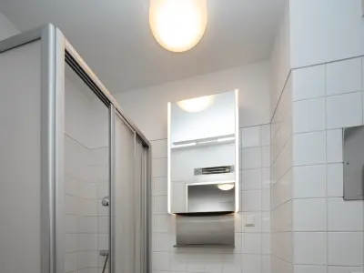 Modernes Badezimmer mit weiß gefliesten Wänden, beleuchtetem Spiegel, Duschkabine mit Glastür und schlichter Deckeleuchte.