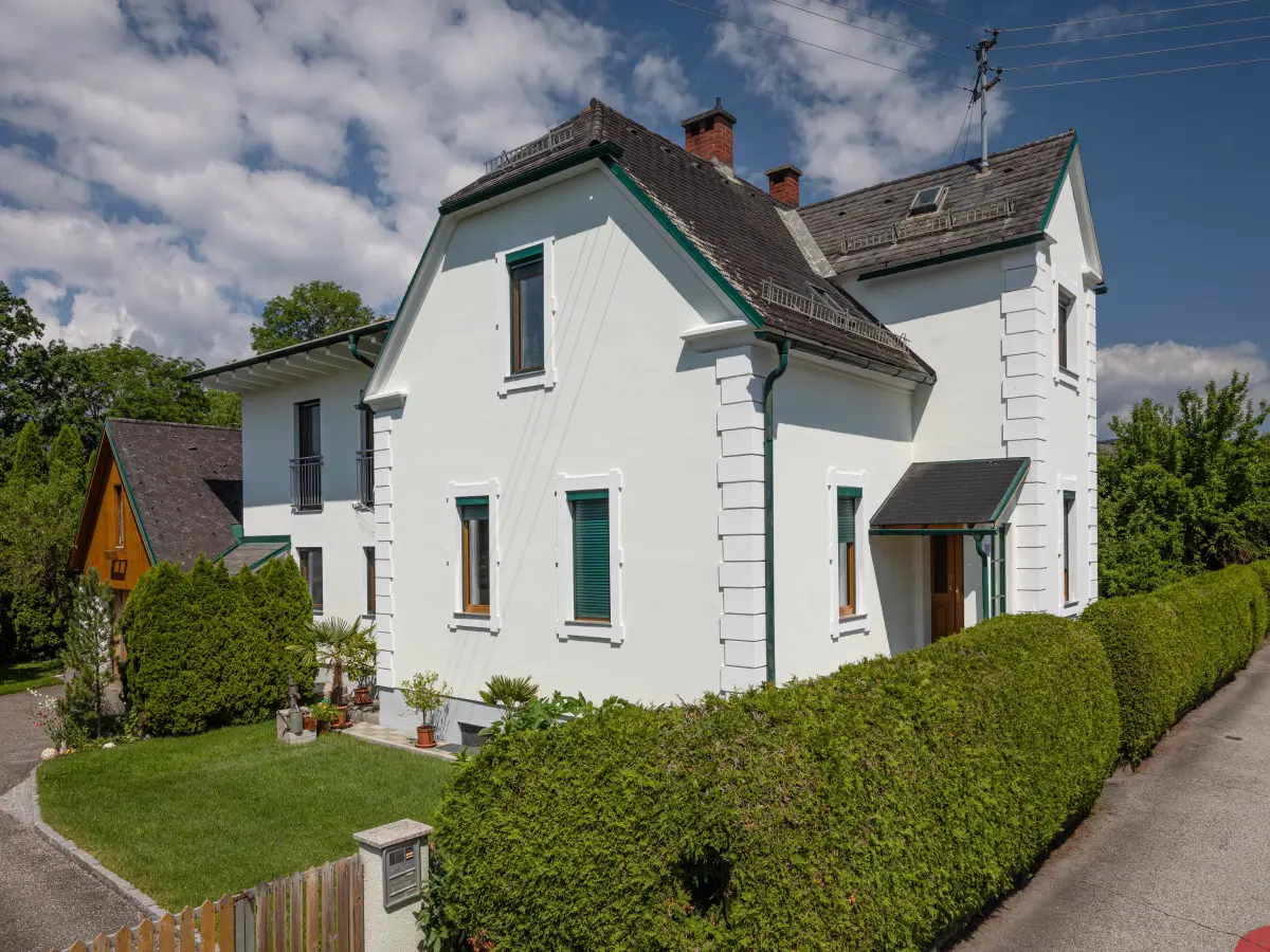 Ein weißes Haus mit grünen Akzenten, umgeben von gepflegten Hecken und Rasen.