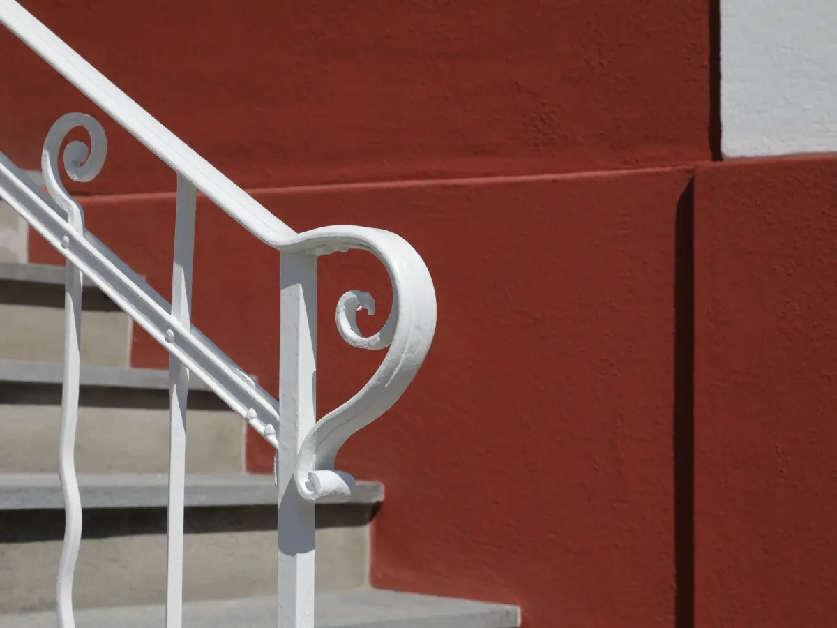 Detailansicht einer Treppe mit weißem geschwungenem Geländer vor einer roten Fassade.