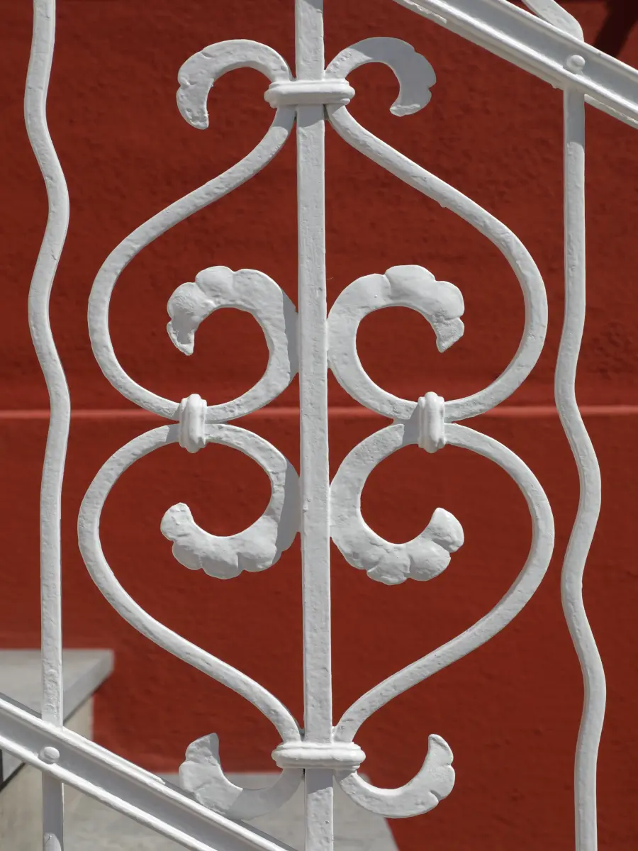 Nahaufnahme eines kunstvoll verzierten weißen schmiedeeisernen Geländers vor einer roten Wand.