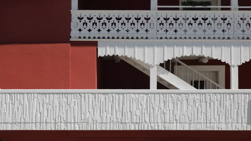 Detail einer roten Fassade mit kunstvoll verzierten weißen Holzbalkonen und dekorativen architektonischen Elementen.