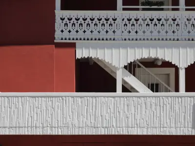 Detail einer roten Fassade mit kunstvoll verzierten weißen Holzbalkonen und dekorativen architektonischen Elementen.