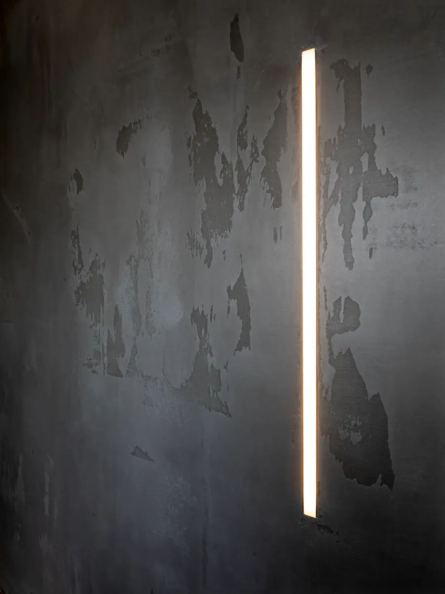 Schlichte Wand mit dunklem Strukturputz und vertikalem, schmalem Wandlicht.