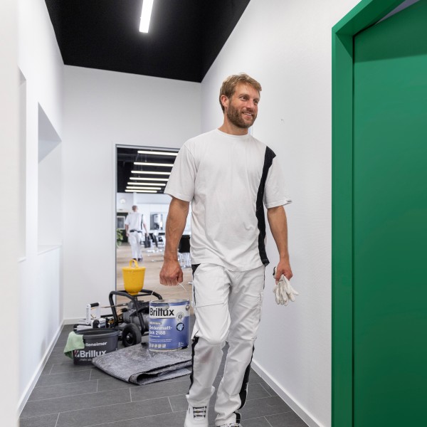 Ein Maler trägt ein Gebinde Hydro-PU-Spray Seidenmattlack 2188 auf einer Baustelle.