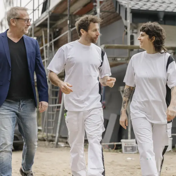 Bauleiter und zwei Maler unterhalten sich vor einem Gebäude mit Gerüst
