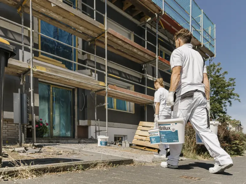 Maler und Malerin tragen Farbeimer zum Haus mit Gerüst