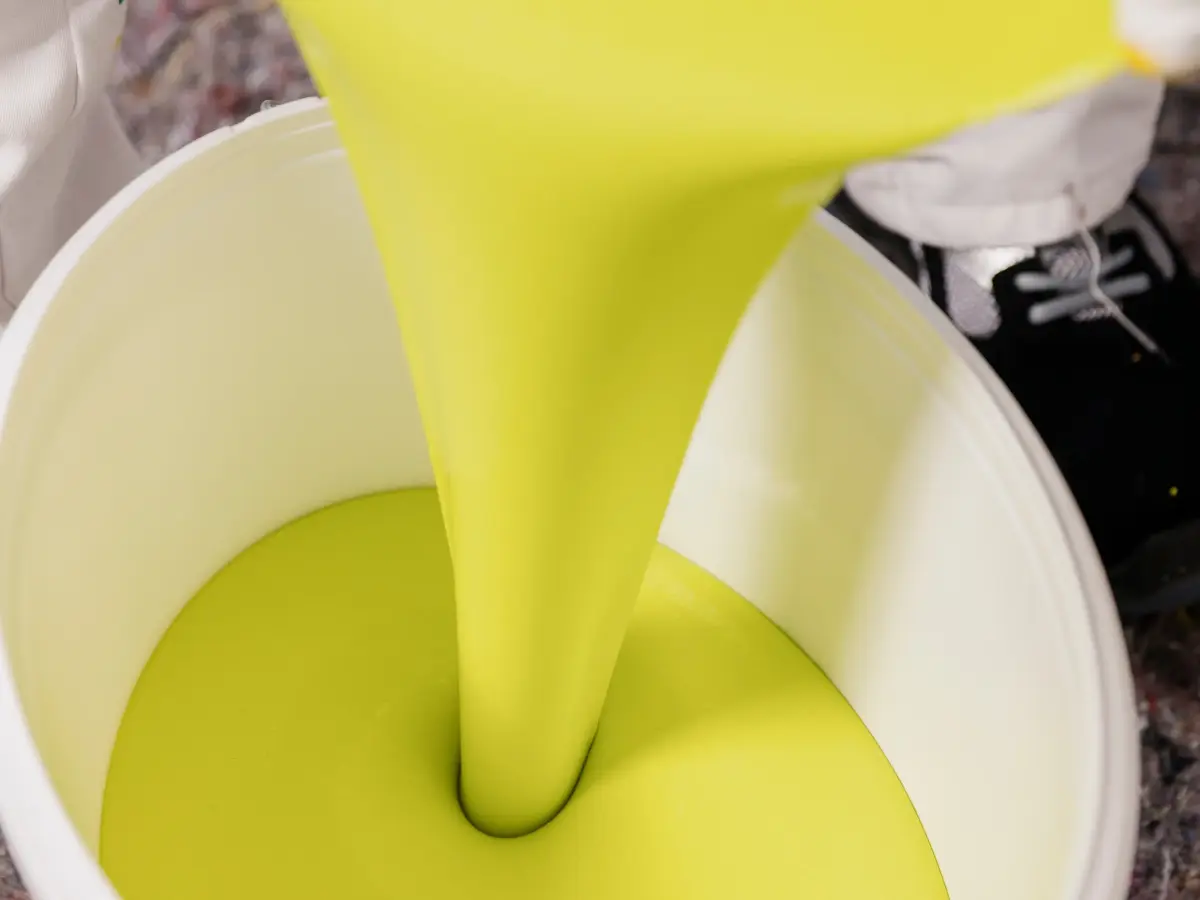 Gele Farbe, die in einen Eimer abgefüllt wird.