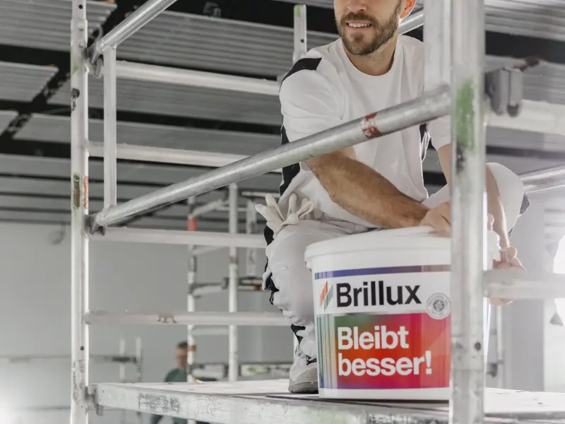 Ein Maler sitzt mit einem Eimer Farbe auf einem Gerüst