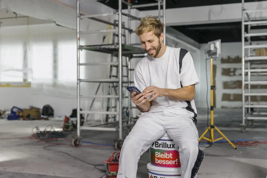 Brillux-Mitarbeiter sitzt auf einem Eimer und schaut auf sein Telefon